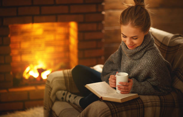 giovane donna che legge un libro vicino al camino in una sera d'inverno - 7650 foto e immagini stock