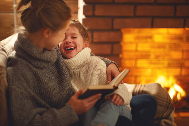 filha de mãe e criança família feliz ler livro na noite de inverno perto da lareira - 7651 - fotografias e filmes do acervo