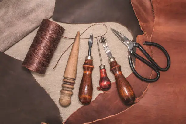 Tools for leather crafting and pieces of brown leather. Manufacture of leather goods. View from above