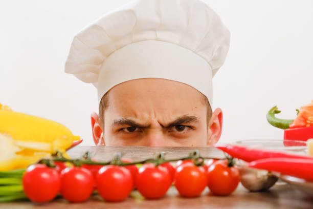 istock Man with cook cap on white background. Chef with vegetables on table. Cook with cheerful face in face close up. 911686942