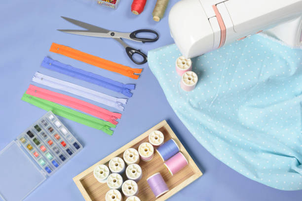 istock Fabrics on sewing machine amid the scissors, shirt buttons, zipper, pin and colorful thread rolls for sewing on blue background, Sewing and needlework concept. 911686968