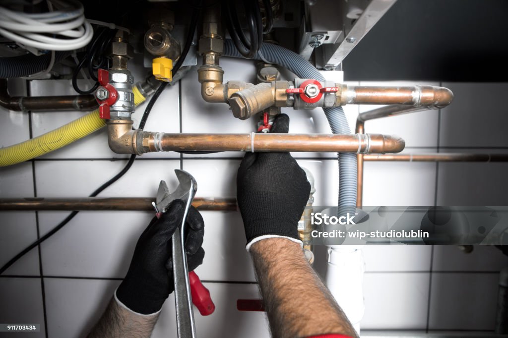 Hands of Plumber with a wrench plumber working at home, work at the heating installation Plumber Stock Photo