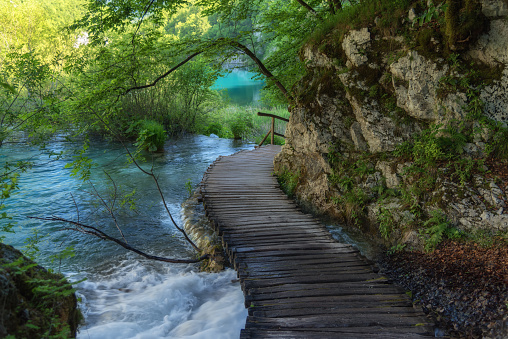 Beautiful view of waterfalls with turquoise water and wooden pathway through over water. Plitvice Lakes National Park, Croatia. Famous attraction, summer landscape.