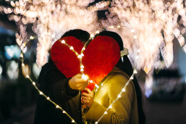A Japanese couple is kissing each other behind a heart shape.