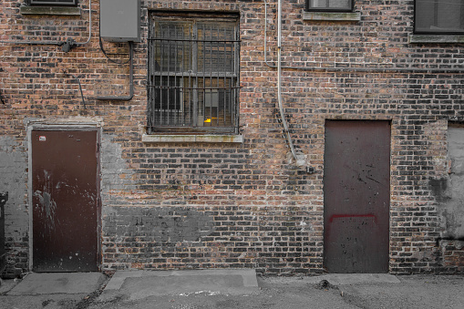 Brick wall with brown doors and barred window in alleyway