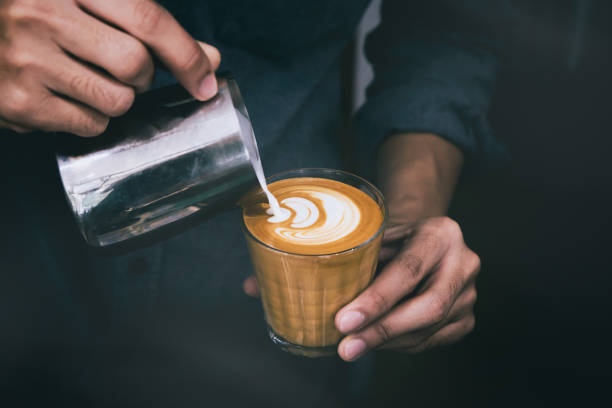 gros plan de barista mâles tenant à la main et coulée de lait chaud pour préparer latte art sur latte piccolo tasse de café. - pouring coffee human hand cup photos et images de collection