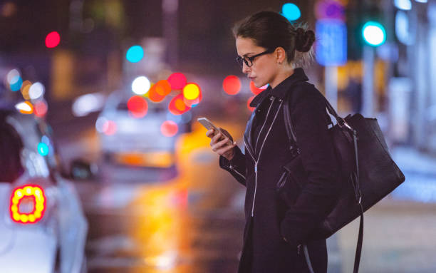 giovane donna che usa lo smartphone per strada della città di notte - walking at night foto e immagini stock