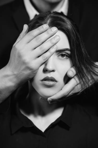 young woman with tie butterfly cover face with palms with drawn eyes, black background, monochrome