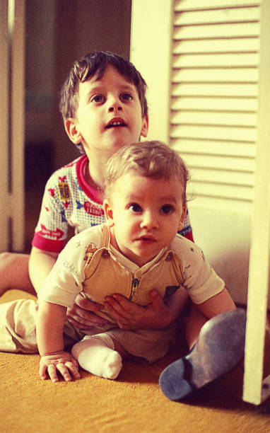 Big brother playing with his baby sister vintage photo from the seventies featuring a boy playing on the floor and  hugging his baby sister at home. brother photos stock pictures, royalty-free photos & images