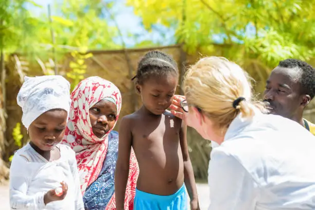 Caucasian female doctor meeting African family with a children.Doctor touching little girl's face