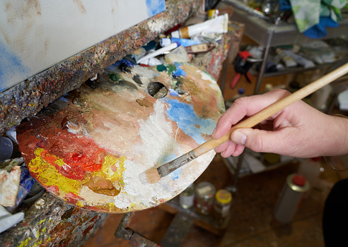 Painters hand holding a paintbrush mixing oil paint.