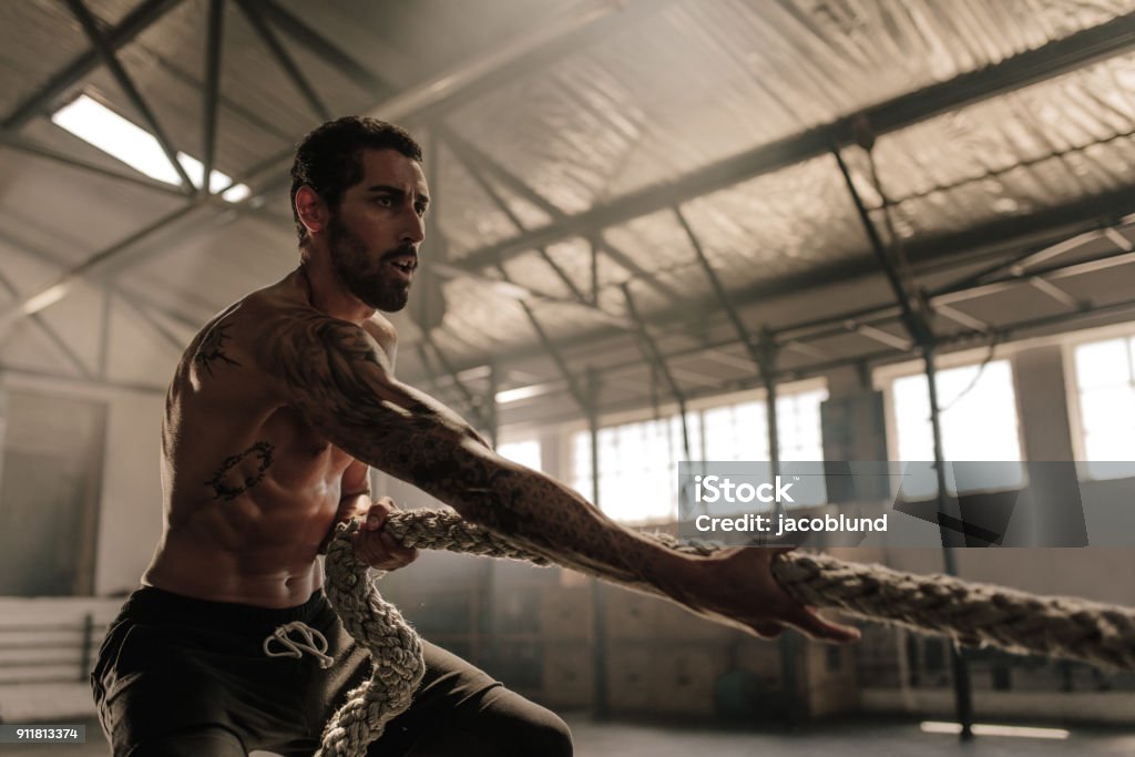 Strong man pulling heavy rope at gym Strong man pulling heavy rope at cross training gym. Male athlete doing exercises with rope at gym. Cross Training Stock Photo