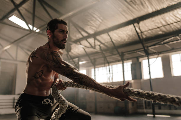 Strong man pulling heavy rope at gym Strong man pulling heavy rope at cross training gym. Male athlete doing exercises with rope at gym. gym men africa muscular build stock pictures, royalty-free photos & images