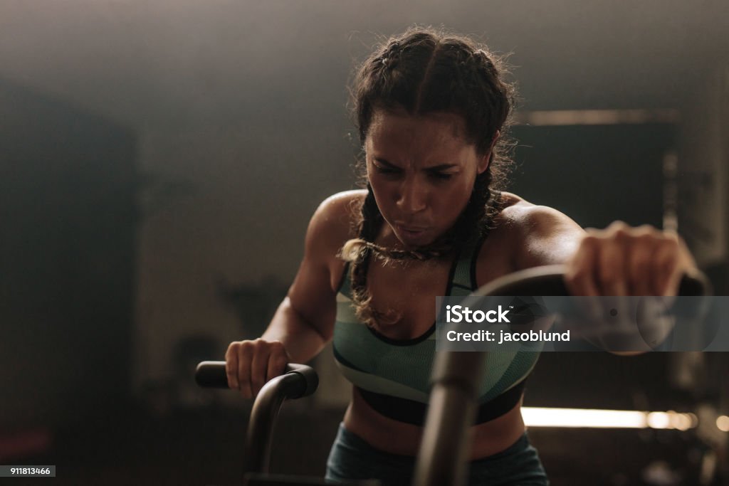 Woman exercising hard on gym bike Woman exercising hard on gym bike. Female using air bike for workout at gym. Effort Stock Photo