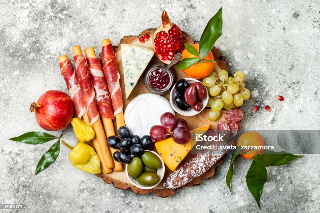 Appetizers table with antipasti snacks. Cheese and meat variety board over grey concrete background. Top view, flat lay Appetizers table with antipasti snacks. Cheese and meat variety board over grey concrete background. Top view, flat lay, copy space Charcuterie Stock Photo