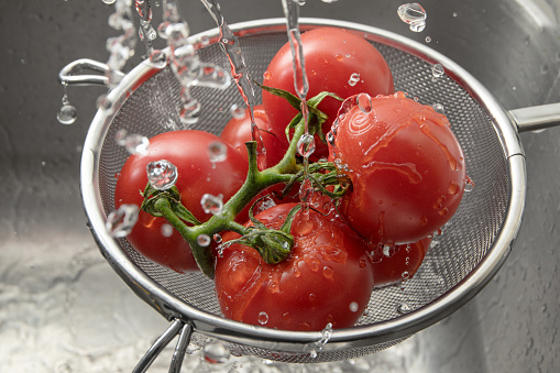 fresh tomatoes in a metal cullender among many drops of water, washing and preparing healthy food