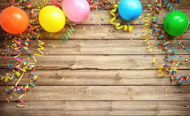 Photo of Colorful carnival or party frame of balloons, streamers and confetti on rustic wooden board