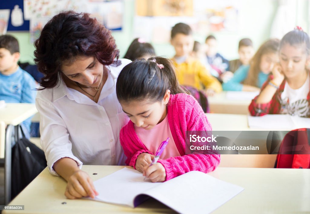 Teacher teaches to write to the girl student in the class Classroom Stock Photo