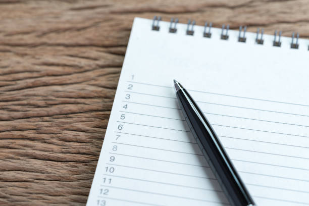 Personal to do lists or work, tasks priority concept, closed up of list of numbers on white clean paper notepad with black pen on wood table in soft tone, organize or writing projects. personal para hacer listas o de trabajo, concepto de prioridad de tareas, cerrado para arriba de la lista de los números en el bloc de notas de papel blanco limpio con lápiz negro en la mesa de madera en tono suave, organizar o proyectos de escritura