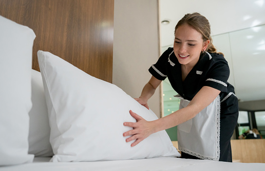 Beautiful housekeeper making the bed at a hotel looking happy and smiling