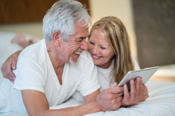 istock Happy senior couple watching videos on a computer tablet laughing and having fun 911864068