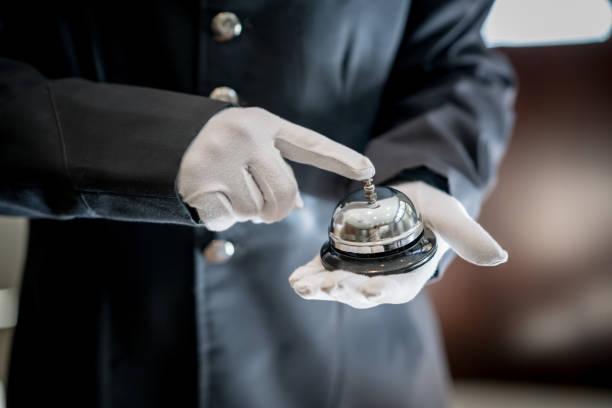 Close up of unrecognizable bell boy at a hotel ringing the bell Close up of unrecognizable bell boy at a hotel ringing the bell using white gloves concierge photos stock pictures, royalty-free photos & images