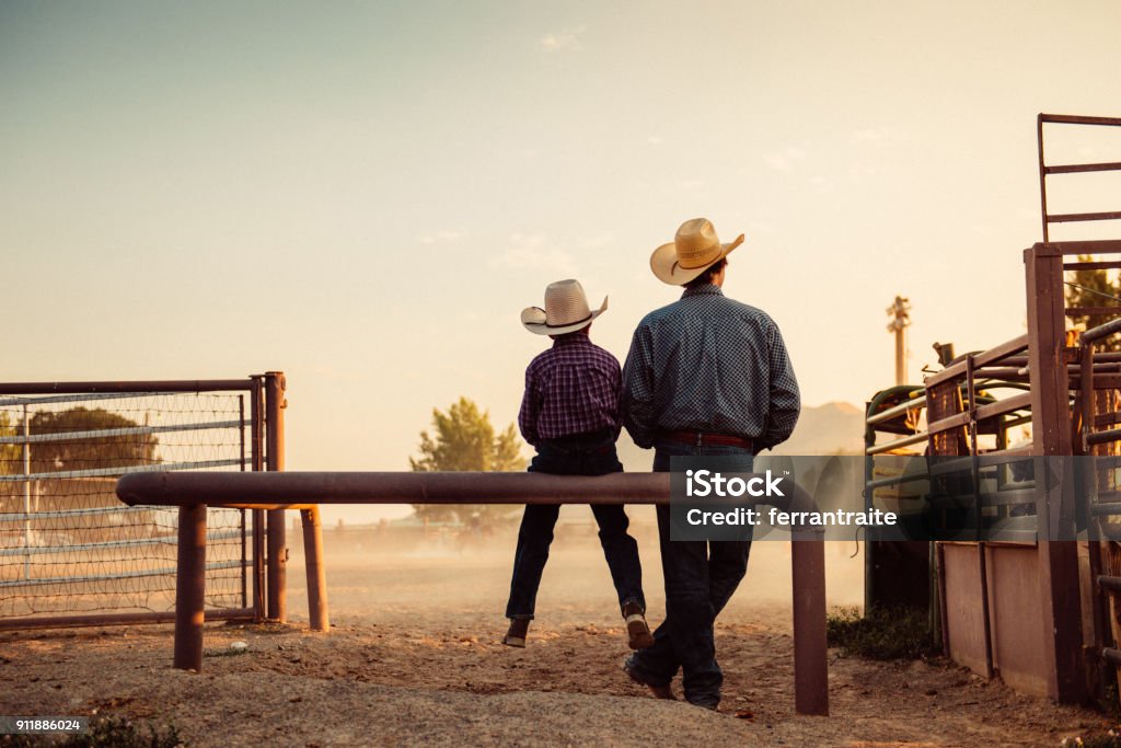 Father and son at rodeo arena Father and son sitting by rodeo arena at sunrise Cowboy Stock Photo