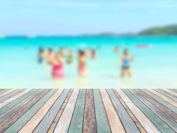 istock Wood table top with blurred people at the beach 911895526