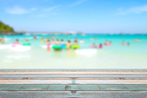 istock Wood table top with blurred people at the beach 911895530