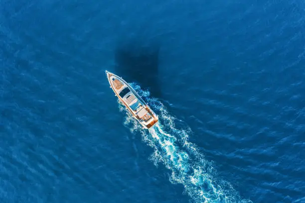 Photo of Yacht at the sea in Europe. Aerial view of luxury floating ship at sunset. Colorful landscape with boat in marina bay, blue sea. Top view from drone of yacht. Luxury cruise. Seascape with motorboat