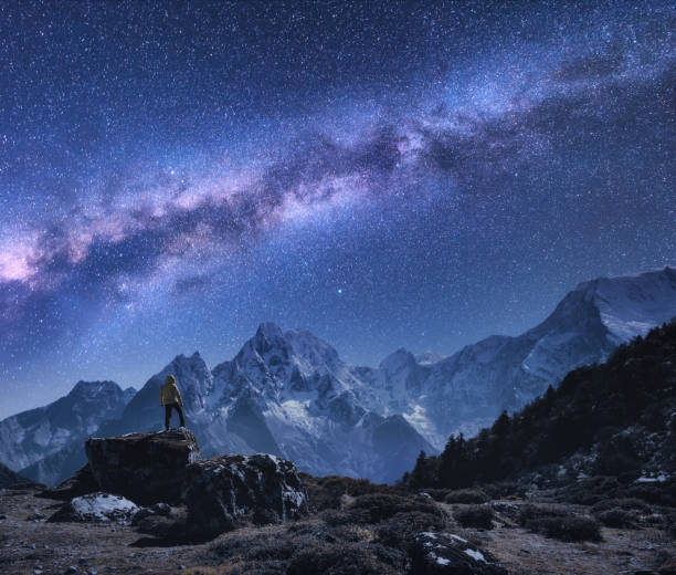 space with milky way and mountains. standing man on the stone, mountains and starry sky at night in nepal. rocks with snowy peaks against sky with stars. trekking.night landscape with bright milky way - himalayas mountain nepal mountain range imagens e fotografias de stock