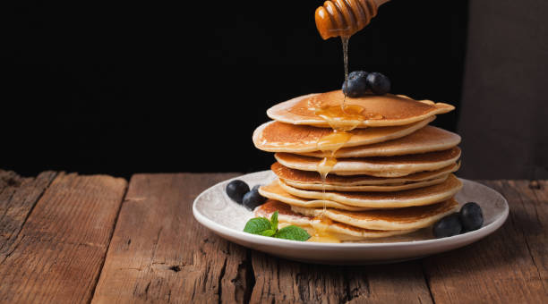 istock The chef pours honey pancake stack with blueberries and mint on black background. Copy space for your text 911905264