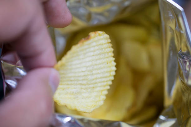 istock hand holding Potato chips from snack bag 911915230