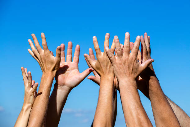 istock Group raising hands against blue sky background, close up 911922108