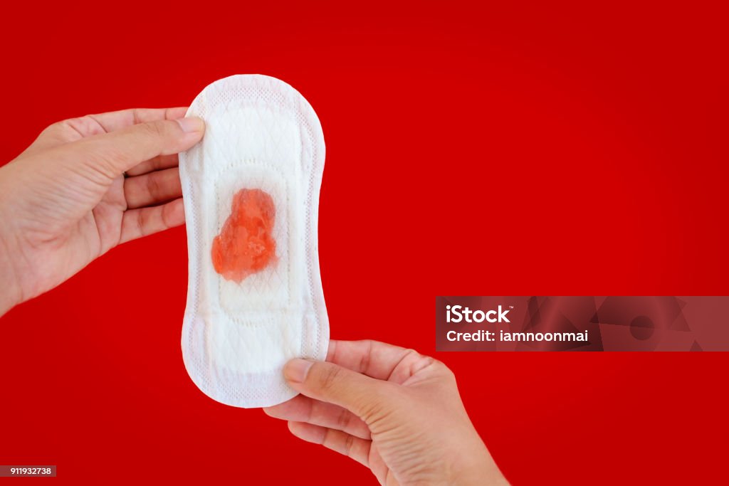 Hand holding feminine sanitary napkin with red liquid drops on red background with copy space  for hygiene and health concept Menstruation Stock Photo