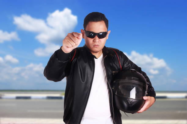 Mature man with sunglasses wearing biker jacket sitting on his motorcycle after a ride in the desert at sunset
