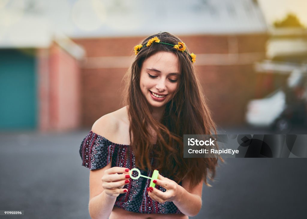 Beautiful teenager blowing bubbles outside holds bubble wand, smiling A lovely smiling young woman with long brown hair gets blown by a breeze as she holds a bubble wand, ready to blow bubbles. Teenager Stock Photo