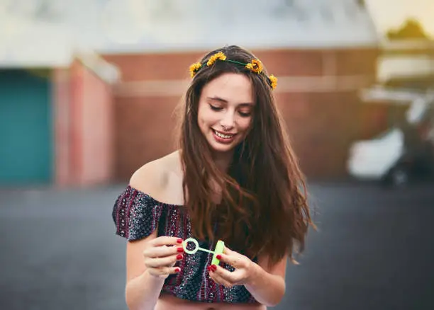 A lovely smiling young woman with long brown hair gets blown by a breeze as she holds a bubble wand, ready to blow bubbles.