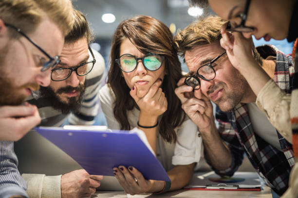 Team of nerdy entrepreneurs reading confusing reports in the office. Group of thoughtful business people with eyeglasses reading documents in the office. confusion stock pictures, royalty-free photos & images