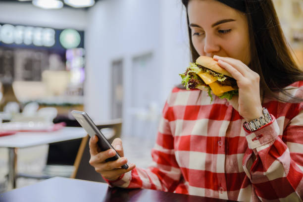 istock woman eat humburger while searfing the phone 911970150