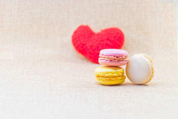 Sweet macaron in cream,yellow and pink violet put overlap with background blurry red heart in crochet and background clear brown, delicious french's biscuite, sweet scene for valentine's day