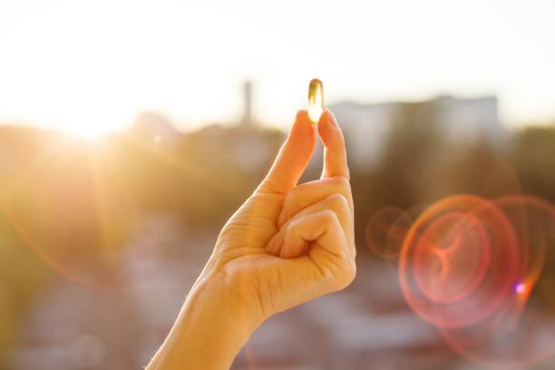 Hand of a woman holding fish oil Omega-3 capsules, urban sunset background. Healthy eating, medicine, health care, food supplements and people concept stock photo