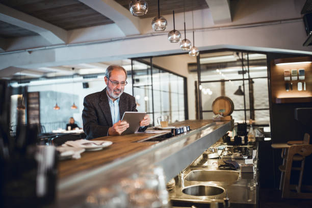 istock Mature businessman working at the bar in high end restaurant. He is using digital tablet 911978046