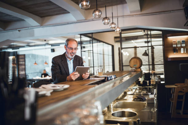 istock Mature businessman working at the bar in high end restaurant. He is using digital tablet 911978058