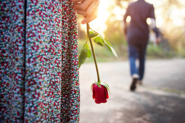 Sadness Love in Ending of Relationship Concept, Broken Heart Woman Standing with a Red Rose on Hand, Blurred Man in Back Side Walking away as background Sadness Love in Ending of Relationship Concept, Broken Heart Woman Standing with a Red Rose on Hand, Blurred Man in Back Side Walking away as background relationship breakup stock pictures, royalty-free photos & images