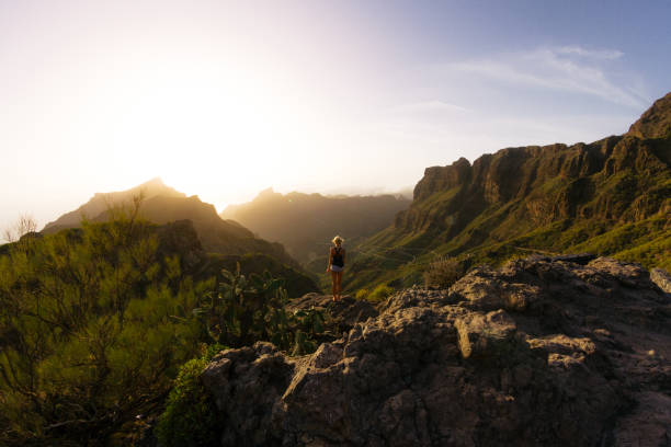 istock Young blond woman in shorts looking at rocky landscape with steep cliffs while sunset 911978320
