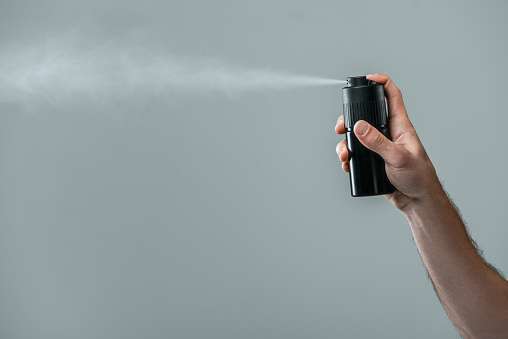 cropped view of man spraying deodorant, isolated on grey with copy space