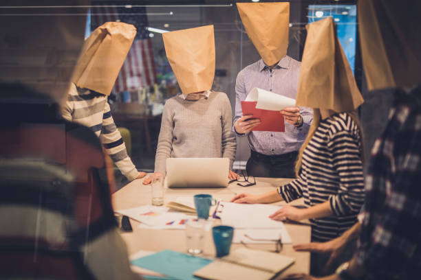 Group of business people with paper bags having a meeting in the office. Large group of entrepreneurs having a business meeting in the office while hiding their faces with paper bags. The view is through glass. staff meeting photos stock pictures, royalty-free photos & images