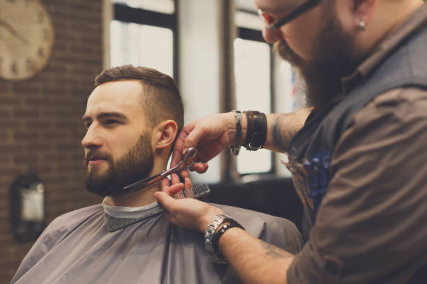 istock Barber styling beard with scissors to client at barbershop 911980572