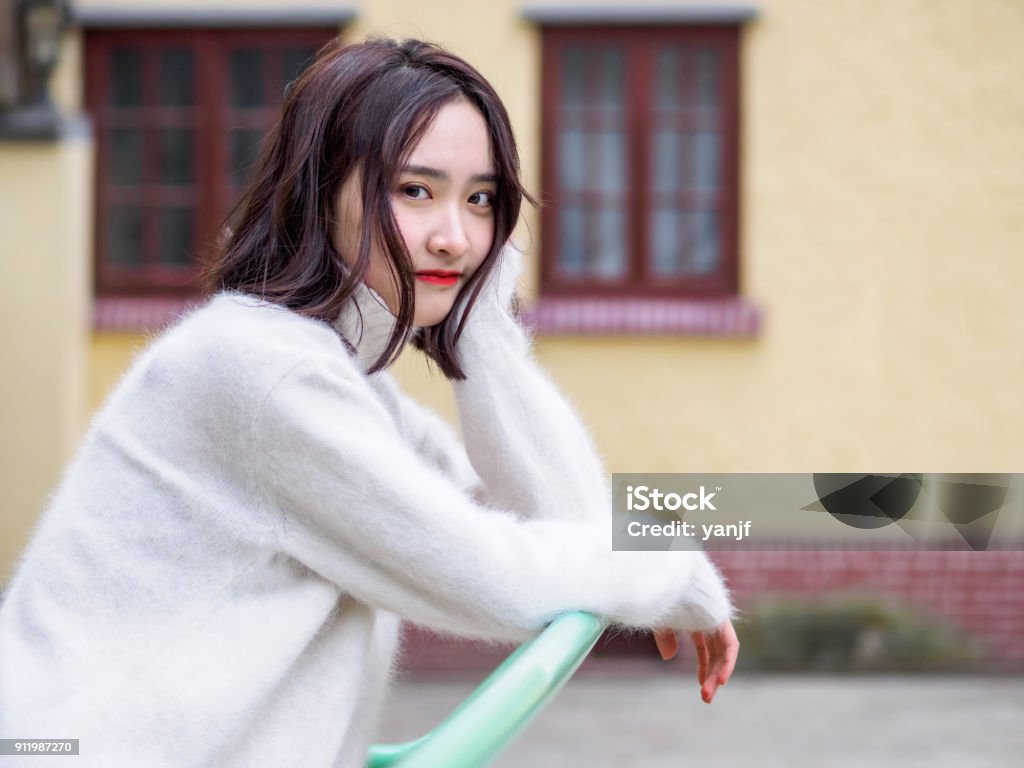 Hermosa mujer morena joven mirando a cámara con desenfoque de fondo de la casa. Retrato de moda al aire libre de glamour joven alegre elegante señora, emociones, personas, belleza y estilo de vida concepto chino. - Foto de stock de Mujer bella libre de derechos